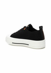 Zapatilla de lona negra con suela de goma blanca, que presenta un ojal naranja y una etiqueta negra con costuras naranjas en el talón.