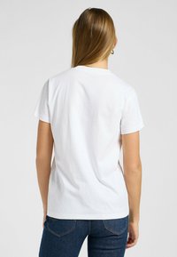Camiseta blanca de algodón con cuello redondo y mangas cortas, que presenta una textura suave y un corte relajado. La vista trasera muestra un detalle mínimo.