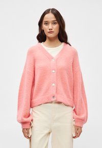 Ροζ πλεκτή κάρντιγκαν με V-λαιμό, μακριά μανίκια μπαλονιού και κλείσιμο με πέντε κουμπιά. Υφασμάτινη υφή, κοντή εφαρμογή και ριμπ μανσέτες.