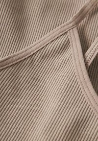 Ingrandimento di un tessuto beige a coste con bordi cuciti e dettagli di fascia sottile su un materiale morbido e testurizzato.