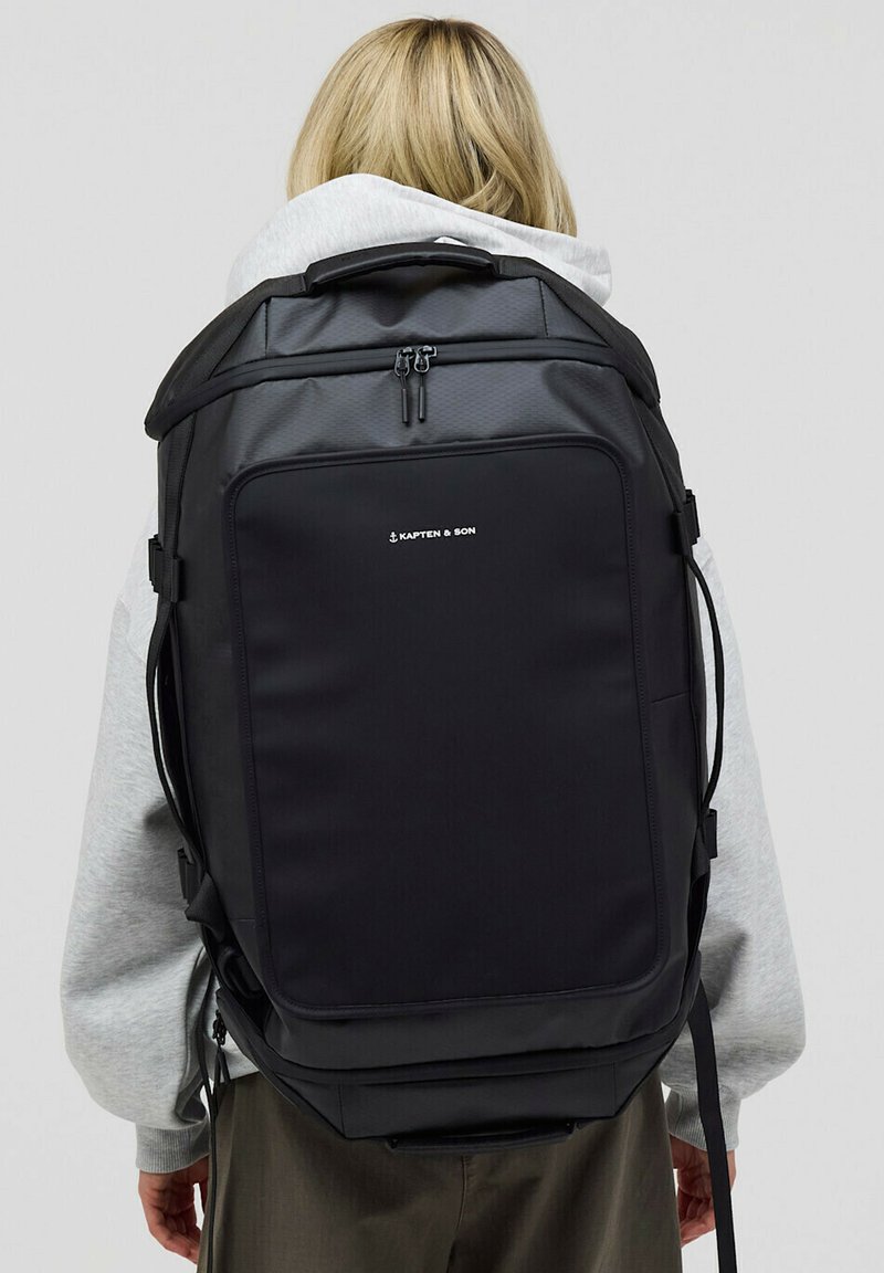 Czarny plecak o strukturalnym kształcie, wykonany z wytrzymałego materiału. Posiada główną komorę na zamek błyskawiczny oraz logo marki z przodu.