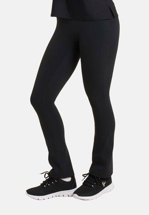 Leggings neri realizzati in tessuto elastico con una superficie liscia, design aderente e cuciture. Abbinati a scarpe sportive nere con suole bianche.