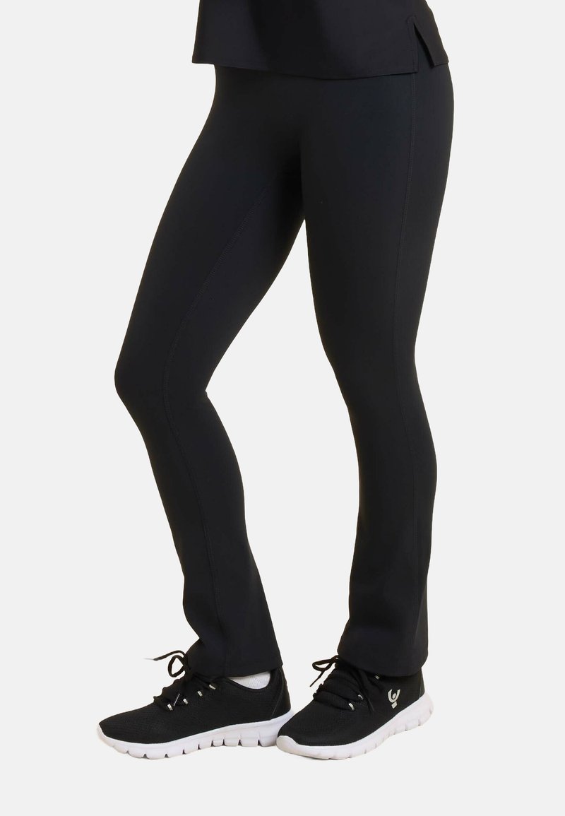 Leggings neri realizzati in tessuto elastico con una superficie liscia, design aderente e cuciture. Abbinati a scarpe sportive nere con suole bianche.