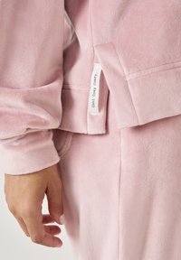 Felpa in pile rosa con una texture morbida, polsini a costine e un piccolo tag con la scritta "cool cosy comfy" cucito di lato.