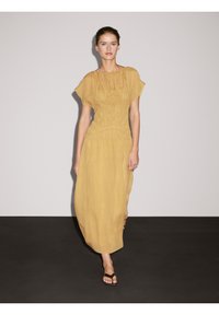 Geel, lichtgewicht, vloeiende maxi-jurk met korte mouwen en geplooide textuur. Beschikt over een gecinchde taille en een ontspannen silhouet.