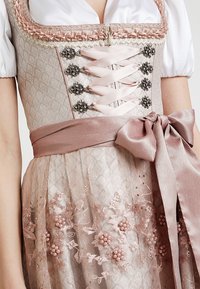 Robe dirndl avec un corsage beige texturé, des lacets en satin rose, des boutons argentés décoratifs et une jupe légère rose en couches ornée de broderies florales.