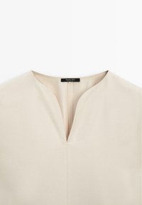 Top beige en V fabriqué en tissu lisse, avec un décolleté en forme de clé et de subtils détails de couture, portant une étiquette "Massimo Dutti."