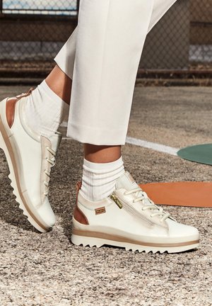 Baskets en cuir blanc avec des accents marron, surface texturée, bout arrondi et semelle épaisse striée. Complète une tenue légère.