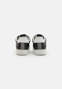 Sneakers in bianco e nero con tomaia in pelle nera texture, dettagli in suede grigio e suola in gomma bianca. La vista posteriore mostra due linguette.