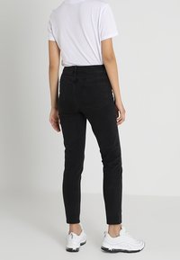 Svarta slim fit jeans med hög midja, subtila sömnadsdetaljer och en slät textur, tillsammans med en vit t-shirt och vita sneakers.