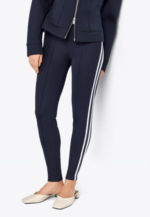 Leggings navy avec des rayures blanches sur les côtés, en tissu lisse et extensible. Associés avec des mules beige à bout carré.