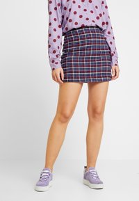 Lila långärmad skjorta med vinröda prickar, kombinerad med en rutig minikjol i marinblått och rött, kompletterad med lavendelfärgade sneakers.