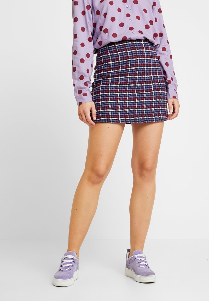 Lila långärmad skjorta med vinröda prickar, kombinerad med en rutig minikjol i marinblått och rött, kompletterad med lavendelfärgade sneakers.