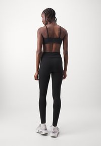 Black sports bra and high-waisted leggings made of stretchy fabric. Smooth texture with minimal seams. Featuring a logo detail on the bra.