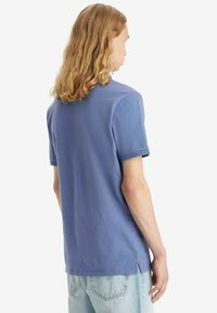 Camicia azzurra a maniche corte in tessuto leggero. Taglio dritto con spacchi laterali. Abbinata a jeans larghi in denim chiaro, per un look rilassato.