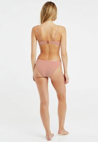 Bikini s červenými a bílými pruhy, s tenkými nastavovacími ramínky a spodním dílem s nízkým pasem. Materiál vypadá hladce a má přiléhavý design.