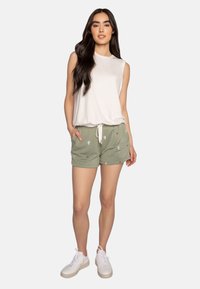 Lichtgrijze mouwloze top, olijfgroene shorts met cactus- en hartborduursel, en witte sneakers met gestructureerde zolen.