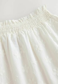 Blouse blanche avec un col smocké et une broderie florale. Tissu léger avec une texture douce. Design fluide.