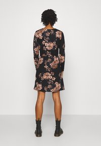 Kwiecista sukienka w kolorze czarnym z brązowymi i niebieskimi kwiatami, z długimi rękawami, okrągłym dekoltem i rozkloszowanym krojem, zestawiona z czarnymi botkami do kostki.