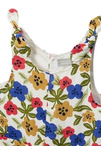 Robe sans manches blanche avec un motif floral rouge, bleu et jaune et des bretelles nouées, comportant une petite étiquette en tissu à l'intérieur de l'encolure.