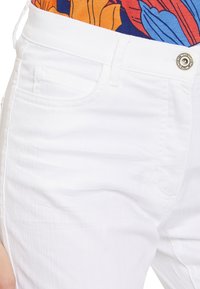 Vita denimbyxor har en strukturerad passform, subtil textur och standardfickor. Midjan har en metallknapp som detalj.