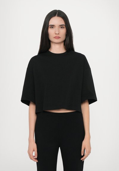 Schwarzes, kurzes T-Shirt aus weichem Stoff mit rundem Halsausschnitt und kurzen Ärmeln, kombiniert mit schwarzen, engen Hosen.