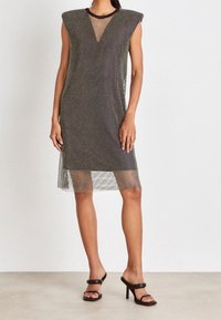 Černé poloprůhledné šaty s puntíkovým vzorem, výstřihem do V, vycpanými rameny a délky po kolena, doplněné černými lodičkami na vysokém podpatku.