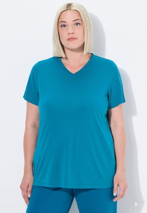 T-shirt teal con scollo a V, maniche corte e vestibilità ampia. Tessuto morbido e texture liscia, abbinato a pantaloni teal coordinati.