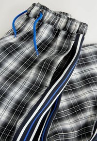 Jogging en plaid noir et blanc avec une taille à cordon, ornés de touches de bleu sur les rayures latérales. Fabriqués en tissu doux avec un motif texturé.