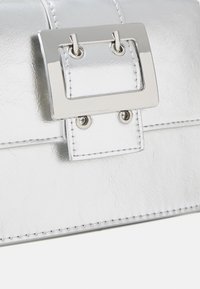 Silver metallic handbag with a glossy finish, featuring a rectangular silver clasp, stitching details, and two circular hardware accents.