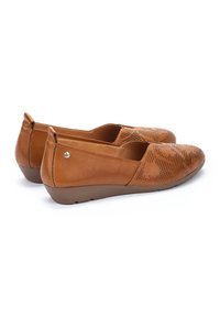 Ballerines en cuir marron avec un design perforé et un bout arrondi. Talon en caoutchouc bas et texture lisse, avec un accent métallique subtil.