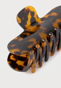 Κλιπ μαλλιών σε σχέδιο φολίδας χελώνας από γυαλιστερό πλαστικό. Διαθέτει στρογγυλεμένη κορυφή και επιμήκη δόντια για ασφαλή κράτημα των μαλλιών. Λείο, γυαλιστερό υλικό.