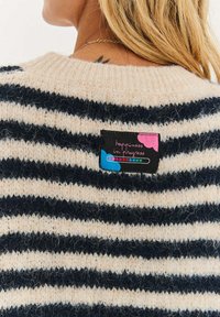 Sweter w paski w kolorze kremowym i granatowym, wykonany z miękkiego, puszystego materiału, z metką z napisem „szczęście w trakcie”.