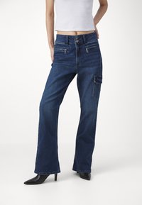 Mörkblå vida jeans i denim med hög midja, framfickor och en sidoficka för cargo. Matchas med svarta spetsiga klackar.