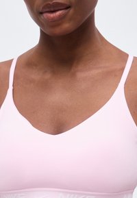 Gros plan du cou et du haut de la poitrine d'une femme portant un soutien-gorge de sport Nike rose clair avec de fines bretelles.