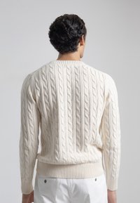 Suéter de punto trenzado texturizado en crema, con cuello redondo y puños acanalados, de diseño ajustado que se estrecha en la cintura.