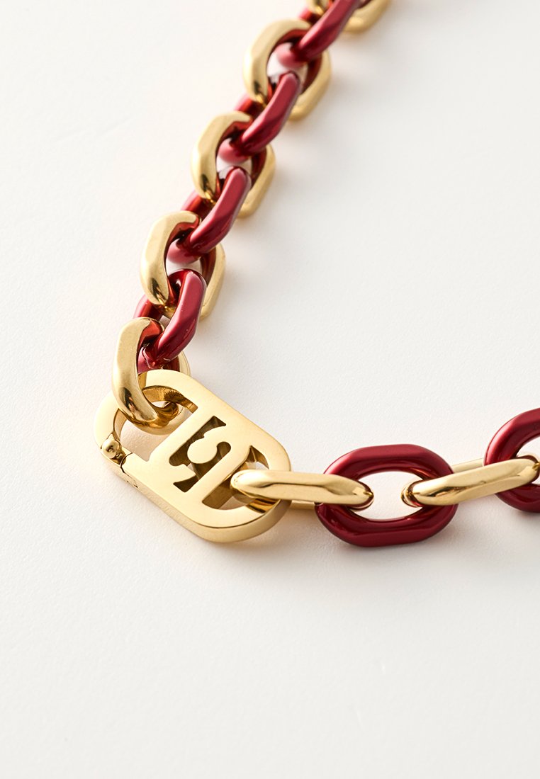 Masywna naszyjnik z łańcuchem z naprzemiennymi złotymi i czerwonymi ogniwami oraz złotym zapięciem z wyciętym wzorem.