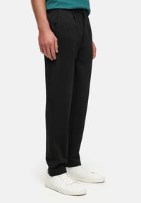 Pantaloni neri su misura con un design a gamba dritta, realizzati in tessuto liscio. Abbinati a sneakers bianche e una maglietta teal visibile in cima.