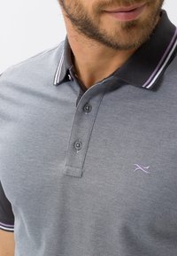 Polo gris avec un tissu texturé, comprenant une patte de boutonnage à deux boutons, un col rayé violet et blanc, et un logo subtil sur la poitrine.