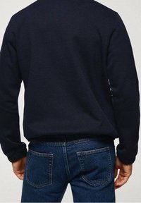 Felpa blu navy lavorata a maglia con maniche lunghe, polsini e orlo a coste, abbinata a jeans in denim a lavaggio medio con classiche tasche posteriori.