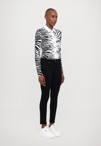 Camisa de manga larga a rayas en blanco y negro con cuello, combinada con jeans ajustados negros y zapatillas blancas.
