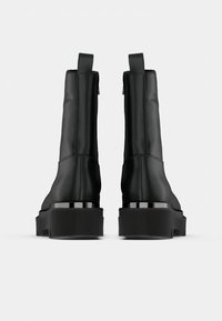 Μαύρα μποτάκια μέχρι τον αστράγαλο από λεία υλικά με χοντρή σόλα και μεταλλική λεπτομέρεια στη φτέρνα, με φερμουάρ και θηλιά έλξης.