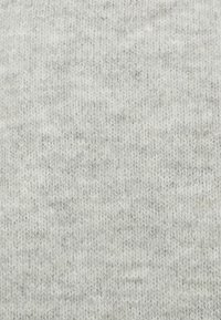 Tissu tricoté gris clair à la texture douce, présentant de subtiles variations de teinte et un motif uniforme de mailles entrelacées.