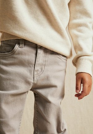 Beiger Pullover mit strukturiertem Strick, kombiniert mit hellgrauen Jeans im klassischen Schnitt und dezenten vertikalen Streifen.