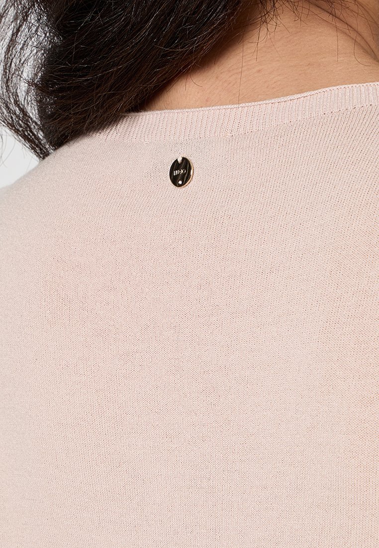 Helles rosa Sweatshirt mit glatter Textur, das an der Rückseite des Halsausschnitts ein kleines Schwarz-Gold-Logo-Detail aufweist. Einfaches, minimalistisches Design.