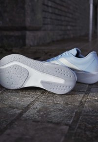 Zapatillas deportivas de color azul claro con una parte superior texturizada, suela blanca con patrones de tracción y un diseño redondeado.