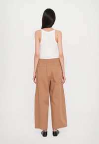 Biała koszulka na ramiączkach w połączeniu z szerokimi brązowymi spodniami. Spodnie mają elastyczny pas i dwie dużie tylne kieszenie. Czarne buty wsuwane.