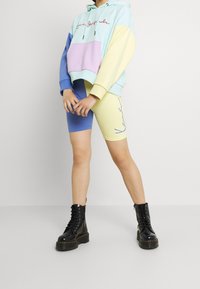 Persona que lleva una sudadera color bloque en tonos pastel y pantalones cortos a juego con un diseño de cara abstracta, combinados con botas de plataforma negras con cordones.