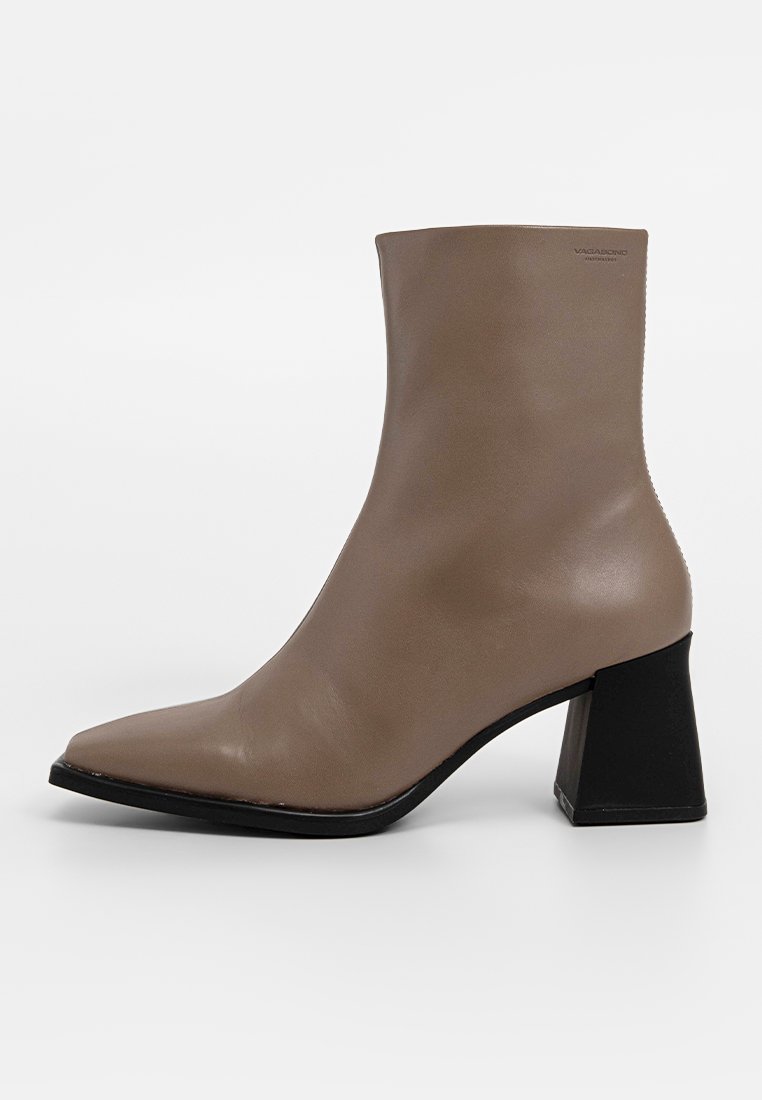 Taupe leren enkelboot met spitse neus en brede zwarte blokhak, minimalistisch ontwerp en subtiel logo nabij de bovenrand.