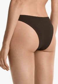 Rjav teksturiran bikini spodnji del z visoko izrezom in minimalno pokritostjo, ki vključuje gladko pasa in tkano vzorčenje. 